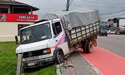 Motorista de caminhão perde a direção, sobe em calçada e colide contra cerca