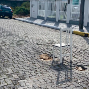 Moradores usam cadeira para sinalizar buracos em via